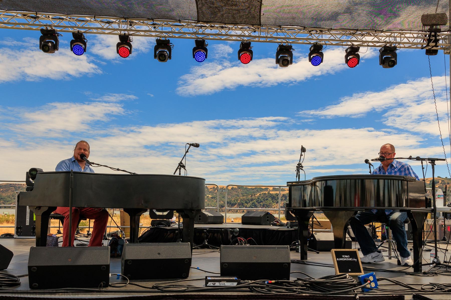 Outdoor festival stage with dueling pianos, lighting truss, and live performers